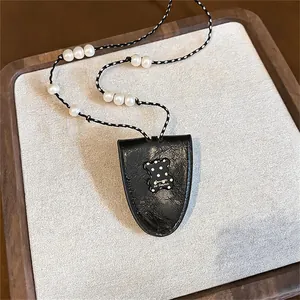 Detailed view of black leather pendant featuring a polka-dot bear and white pearl cord