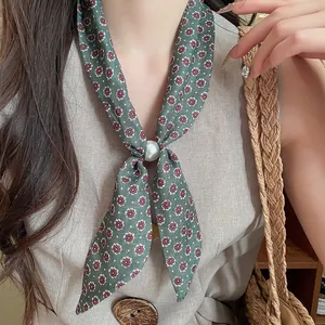 Primer plano de un collar pañuelo de lino con flores vintage y anillo de perlas.