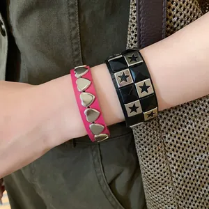 Detailed view of pink heart-studded and black star-studded leather bracelets on wrist.