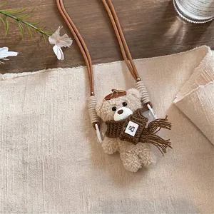 Simpatico ciondolo per telefono in peluche con orsetto e sciarpa marrone su sfondo lino