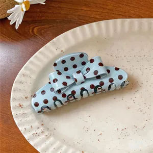 Vintage light blue polka dot acrylic hair claw clip with bow design on ceramic plate