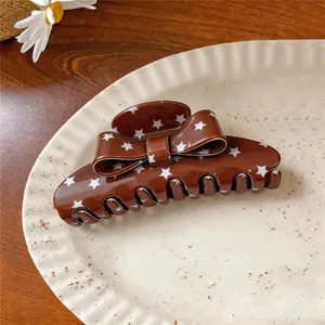 Close-up of brown acrylic bow hair claw clip with white star patterns on a plate