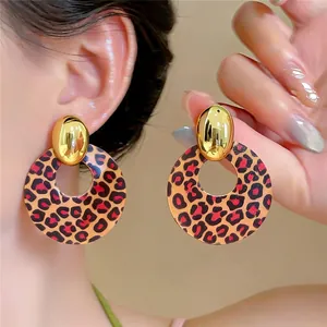 Nahaufnahme ethnischer Holzohrringe mit Vintage-Leopardenmuster und goldenem Detail.