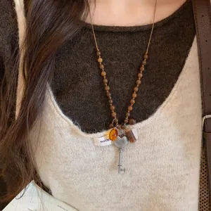 Nahaufnahme einer Holzperlenkette im Ethno-Stil mit Herz-Schlüssel-Anhänger auf Pullover