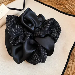 Dettaglio ravvicinato di un grande elastico scrunchie in raso nero a pois bianchi