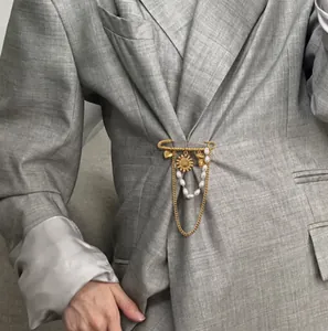 Dettaglio di spilla in acciaio inossidabile dorato con girasole e nappa su blazer grigio