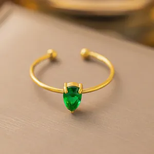 Vista macro di un anello aperto in acciaio dorato con gemma verde a forma di pera