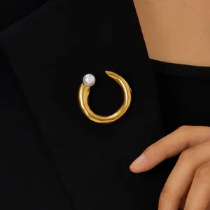 Detail of a minimalist gold-plated stainless steel C-shaped brooch with a pearl on a blazer.