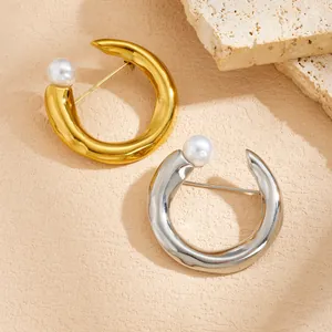 Detail view of gold and silver stainless steel C-shape brooches with pearl accents.