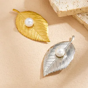 Detailed view of gold and silver leaf brooches with central pearls on stone background