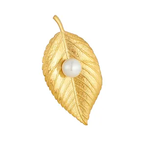 Macro view of a gold-plated stainless steel leaf brooch with a central pearl detail.