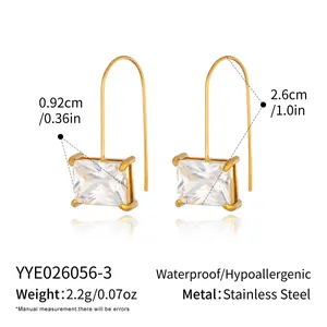 Vista macro de pendientes rectangulares de acero dorado con circón y medidas claras.