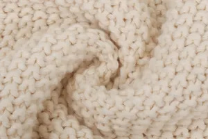Detailed macro view showing the texture of a cream thick cable knit sweater fabric.