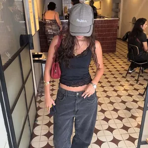 Model wearing a black slim-fit camisole with lace trim in a stylish cafe setting