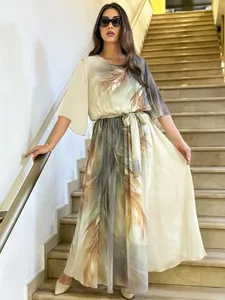 Elegante abito lungo stampato con motivo a piume su modella in posa sulle scale