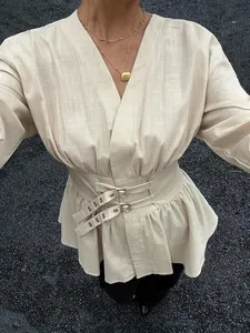 Dettaglio di una camicetta beige retrò con scollo a V, fascia in vita e fibbie metalliche.