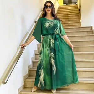 Elegante abito lungo con stampa floreale verde e cintura, presentato su una scala interna.