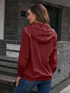 Stilvolle Rückansicht einer bordeauxroten Kapuzen-Regenjacke für Damen im Freien
