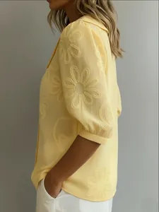 Détail d'une blouse jaune avec broderie florale délicate sur manches bouffantes d'été.