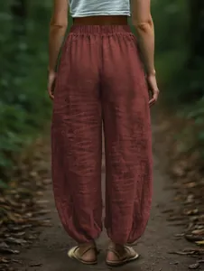 Detailed back view of loose brick red linen-style lantern pants on a forest path