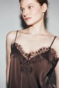 Close-up detail of brown satin camisole with asymmetric black lace trim and silk texture