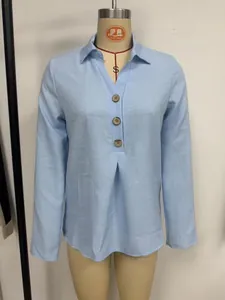 Close-up detail of a light blue long-sleeved shirt featuring wooden buttons and front pleats