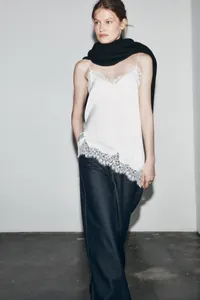 Detail of white asymmetric camisole with delicate lace trim and silk-like fabric