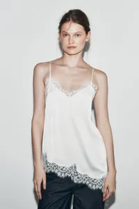 Detailed studio shot of a white silk camisole featuring delicate asymmetric lace trim