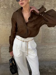 Detalle de una blusa marrón con mangas de linterna y pantalones blancos