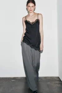 Detailed view of a black asymmetric camisole featuring delicate lace trim on a model.