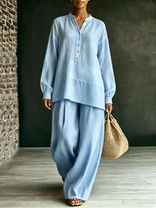 Elegant lichtblauw tweedelig pak met los shirt met lange mouwen en wijde broekspijpen.