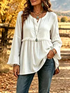 Detail view of a white boho-style long-sleeve blouse with fringe accents and V-neck.