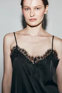 Detailed view of elegant black satin camisole with delicate lace trim along neckline.