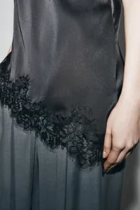 Close-up detail showing the delicate black lace trim on an asymmetrical satin camisole top