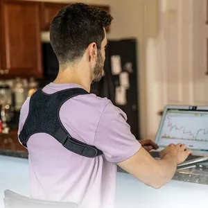 Ergonomic black adjustable back posture corrector worn by a man while using a laptop at home