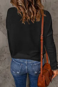 Detailed back view of a women's black long-sleeve knit sweater with a textured wall background