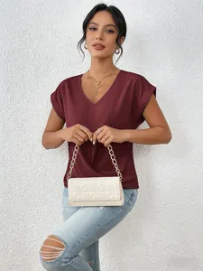 Elegant burgundy V-neck short sleeve top styled with a cream quilted bag and denim jeans.