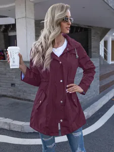 Detailed shot of a women's burgundy hooded raincoat styled in an outdoor street setting.