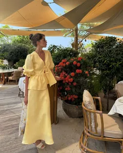 Close-up view of a woman wearing a yellow linen puff sleeve top and midi skirt in a garden