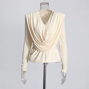 Détail d'un chemisier beige à col bénitier avec épaulettes et plis à la taille.