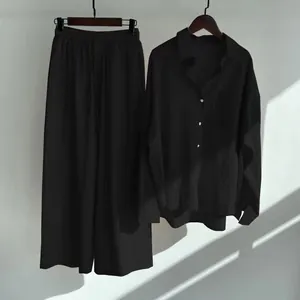 Full view of black cotton linen shirt and wide-leg trousers hanging set on plain wall