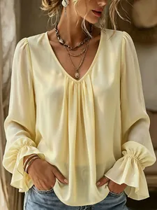 Detail showing elegant V-neck pleated texture and ruffled cuffs of the yellow blouse.