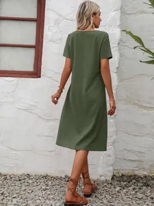 Vue arrière d'une robe midi ample en coton et lin vert devant un mur de pierre blanche.