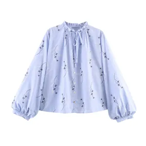 Detailweergave van de ruffelhals en bloemig borduurwerk op deze lichtblauwe blouse.