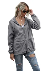 Full view of a woman wearing a grey lightweight hooded rain jacket for outdoor activities.