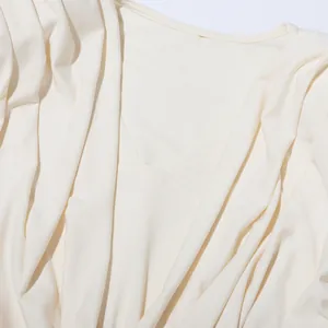 Détail d'un chemisier crème pour femme avec décolleté drapé élégant et tissu plissé.