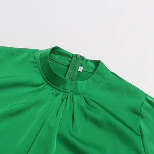 Close-up detail of a bright green satin blouse featuring a pleated stand collar and zipper.