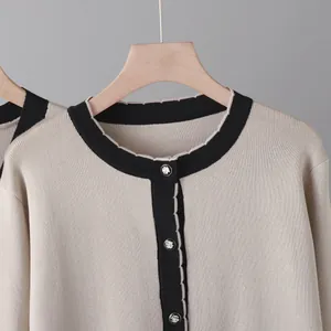 Gros plan sur un cardigan en maille beige chic avec bordure noire et boutons argentés