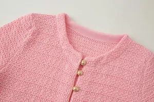 Detailweergave van een roze gebreide top met gouden knopen en een ronde halslijn