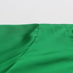 Close-up of green satin blouse showing high-quality stitching and smooth fabric texture.